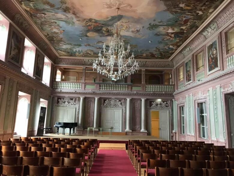 Festsaal mit Kronleuchtern, Sitzreihen und einer Bühne