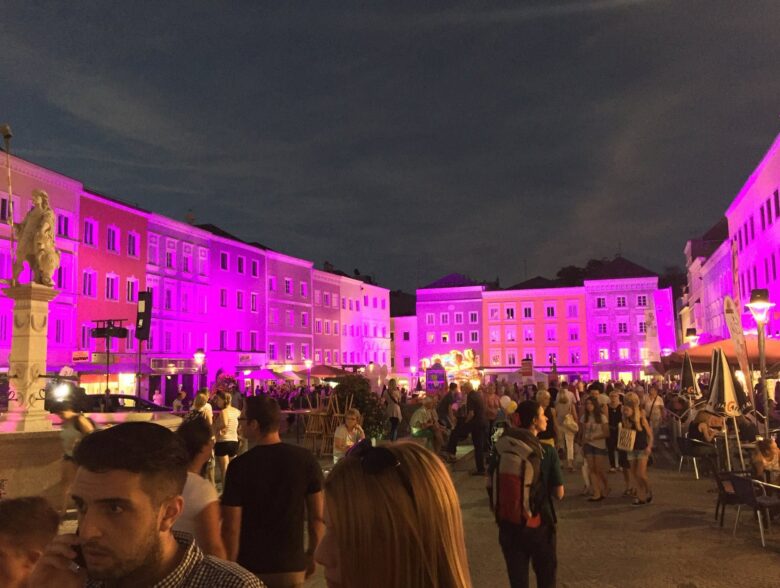 Violett beleuchtete Fassaden und Besucher auf dem Rieder Hauptplatz