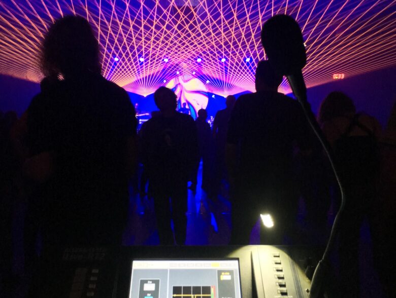Publikum und Tonregie unter farbigen Lichtstrahlen bei einem YAF-Konzert in der Schweiz
