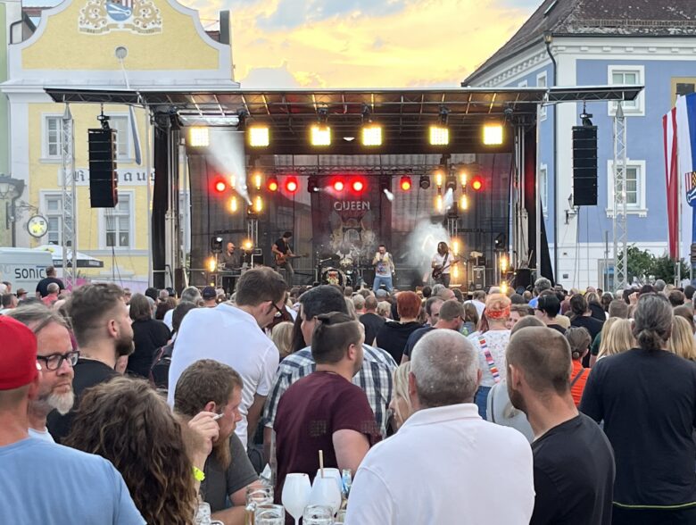 Open-Air-Publikum vor einer beleuchteten Bühne zwischen historischen Fassaden