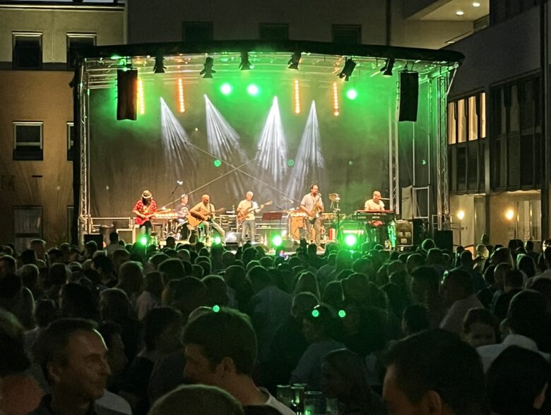 Band auf einer grün und weiß beleuchteten Konzertbühne vor Publikum