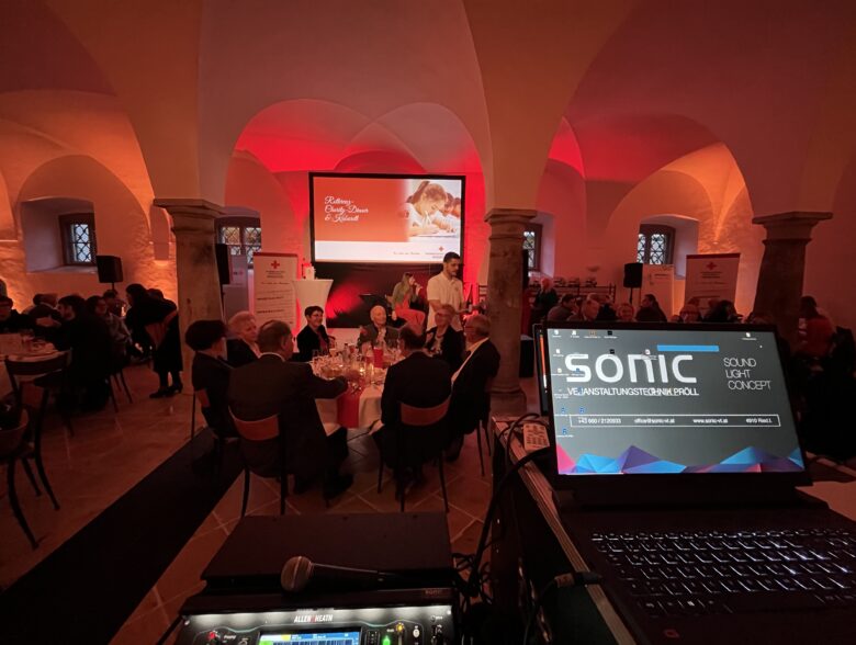 Tonregie vor einer rot beleuchteten Veranstaltung mit Videoleinwand