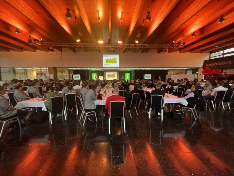 Festlich bestuhlter Saal mit orange beleuchteter Decke und Videoleinwand