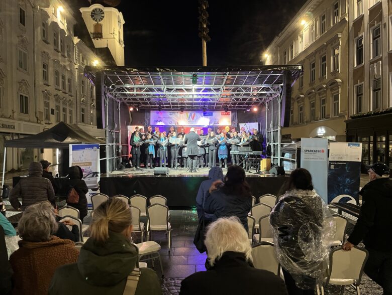 Publikum vor einer beleuchteten Außenbühne zwischen historischen Gebäuden