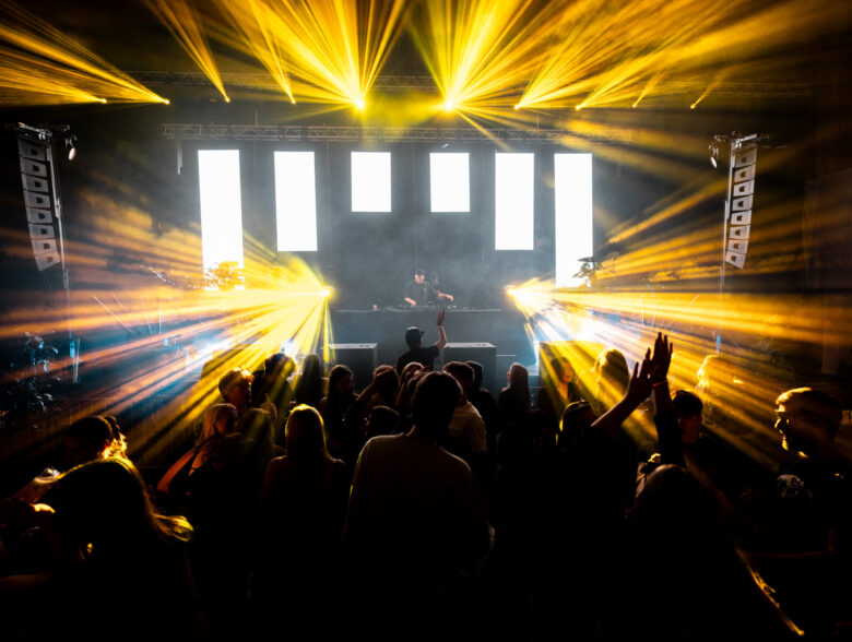 Gelbe Lichtstrahlen und LED-Flächen über der Tanzfläche beim Messe-Clubbing